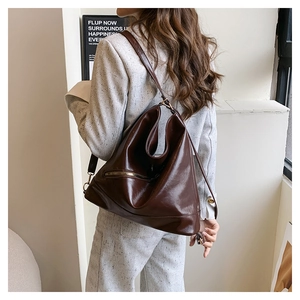 Detail view of large dark brown leather tote bag showing shiny texture and side zipper