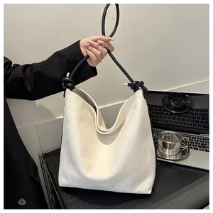 Detail of large beige canvas tote bag with black rope handles and knotted accents