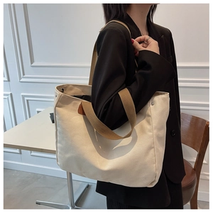 Detail of a beige canvas tote bag showing reinforced metal rivets and brown fabric strap