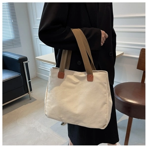 Detail of off-white canvas tote bag with brown straps worn by model for daily commute