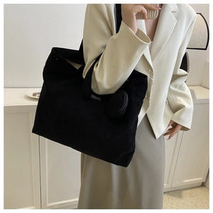 Detail shot of a black corduroy tote bag with round hanging pouch on a beige suit model