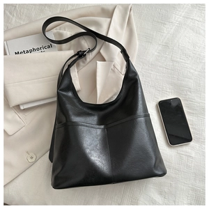 Close-up of black tote bag with front pocket and adjustable strap on a minimalist background