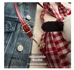 Detail of red checkered nylon bag with adjustable strap, gold buckle and plush charm