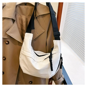 Detail of white nylon crescent bag with black adjustable strap on a classic trench coat