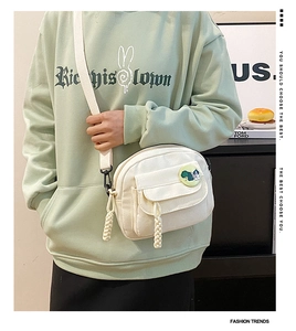 Close-up of white canvas crossbody bag featuring a cute green cartoon dog badge and flap pocket