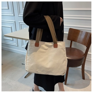 Close-up of cream canvas tote bag showing durable brown woven straps and leather details