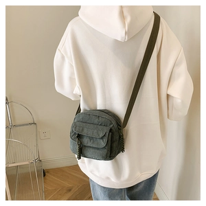 Detail of dark green corduroy crossbody bag with woven knot and flap pocket on cream sweater