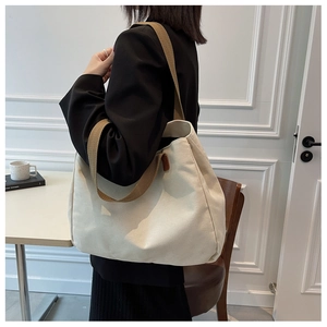 Side view of large canvas tote bag with brown straps worn by model in minimalist room