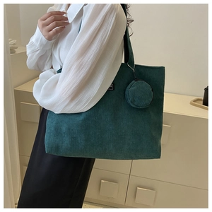 Detail of dark green corduroy tote bag with small round coin pouch on a white shirt model