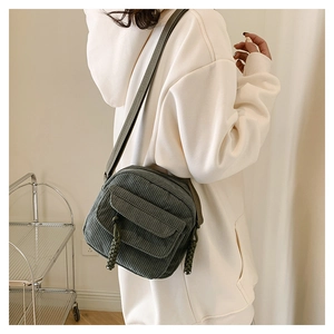 Close-up of dark green corduroy crossbody bag with flap cover and woven rope detail