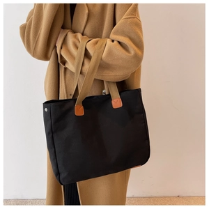 Close-up of black canvas tote bag with leather reinforced handles on a wool coat