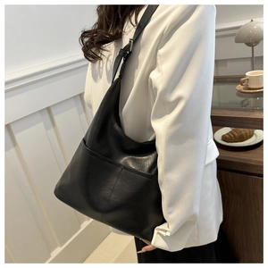 Detail of a minimalist black tote bag with leather texture and adjustable shoulder strap