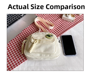 Detail view of cream canvas crossbody bag with small pocket and green cartoon pin