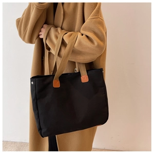 Black canvas tote bag with brown handles on a model wearing a camel wool coat