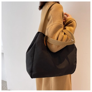 Close-up of a large black canvas tote bag with brown straps worn over a camel wool coat