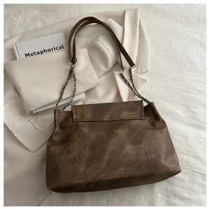 Detailed view of vintage brown textured shoulder bag with metal chain strap on white blazer