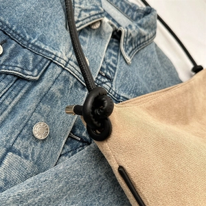 Beige suede bucket bag with stylish knotted black leather shoulder strap and metal accents