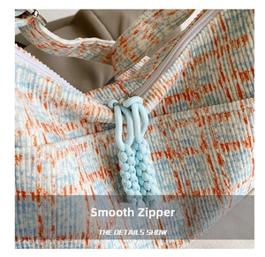Detail of corduroy crossbody bag featuring a blue-orange plaid texture and white zipper