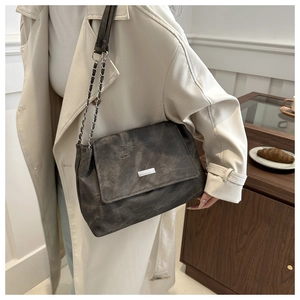 Detail of grey suede shoulder bag with chain strap and metal logo on a model