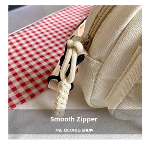 Close-up of a smooth zipper with woven pull cord on a beige canvas shoulder bag