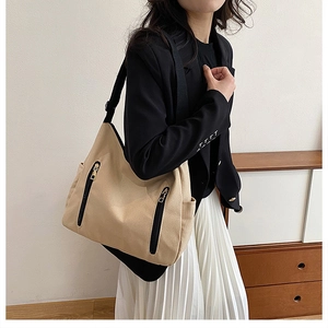 Detail of a large beige canvas tote bag with black wide straps and vertical zip pockets