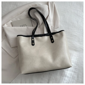 Detail of off-white faux leather tote bag showing textured surface and black shoulder straps