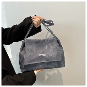 Detail of dark grey tote bag with metal chain strap and minimalist logo on leather flap
