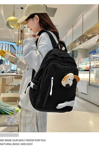 Side view of black corduroy school bag with cartoon dog motif and plush bone detail