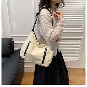Detail of cream canvas shoulder bag featuring dual vertical zippers and black straps