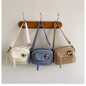 Three canvas crossbody bags in white, blue, and khaki hanging with cute cartoon brooches
