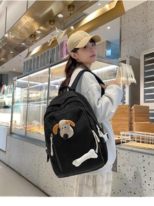 Close-up of black corduroy backpack with 3D plush puppy dog and white bone details