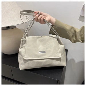 Detail view of beige matte leather texture and elegant metallic logo on a shoulder bag