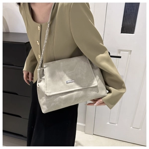 Close-up of light gray suede tote bag with silver chain strap worn by a model in a blazer