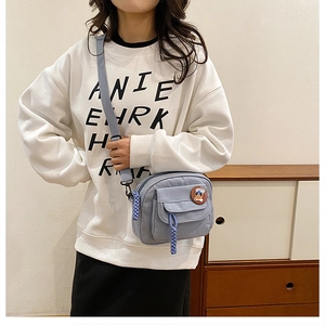 Detail of light blue canvas crossbody bag with cartoon badge and adjustable strap
