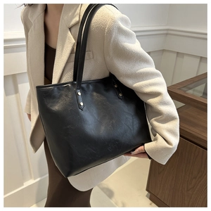 Detail view of black textured PU leather tote bag with gold rivets on cream blazer model