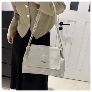 Detail of light beige crossbody bag with silver chain strap and metal logo plaque