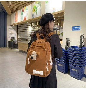 Detailed view of brown corduroy school backpack with 3D plush puppy and bone decoration