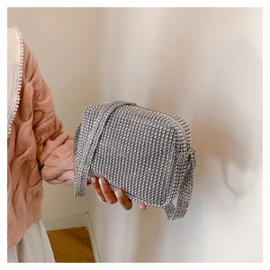 Close-up of a silver rhinestone evening bag with wide shoulder strap held by a model