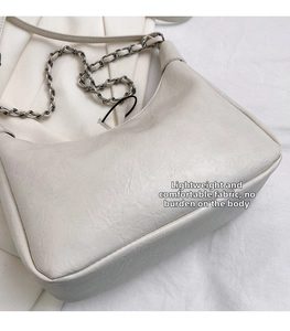 Detail view of cream underarm bag with silver chain strap on soft fabric background
