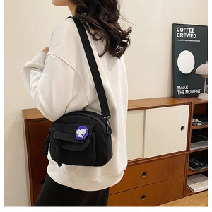 Detail of a black canvas crossbody bag with a blue cartoon badge and wide strap