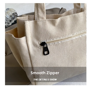Close-up of beige corduroy tote bag showing vertical texture and smooth metal zipper pocket