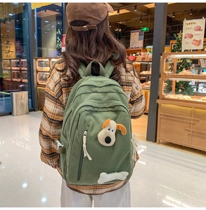Detail of dark green corduroy backpack featuring a cute 3D plush puppy and bone charm