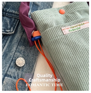 Close-up of green corduroy crossbody bag with orange button and pink woven label detail