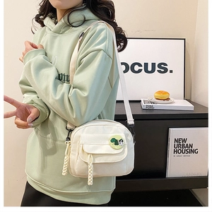 Detail of cream canvas crossbody bag with green cartoon badge and woven zipper pulls