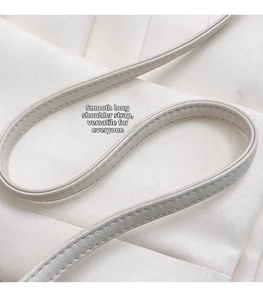 Detail of smooth beige leather shoulder strap with precision stitching on white fabric
