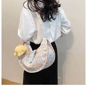Detail of tweed check crescent bag featuring a yellow plush chick charm and wide strap