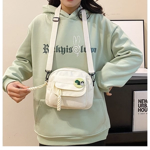 Detail of white canvas crossbody bag with green cartoon badge and adjustable strap