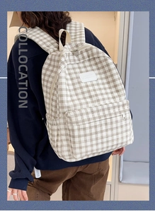 Detail of checkered canvas backpack showing large front zipper pocket and padded straps