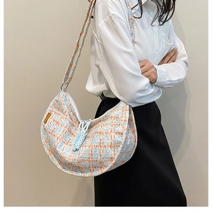Detail of tweed crossbody bag with blue and orange plaid pattern and woven charm