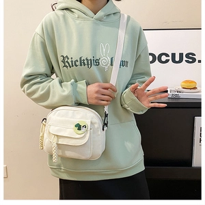 White canvas crossbody bag featuring a front flap pocket and a cute green round badge